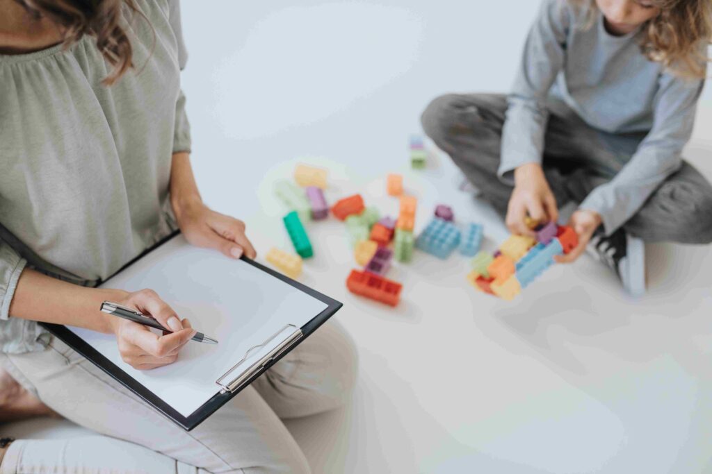 Young female therapist doing notes during session with young autistic boy