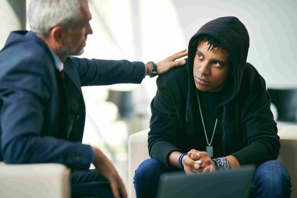 Mature psychotherapist encouraging black male adolescent during therapy at counselling center. Focus is on adolescent.